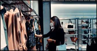 A person with black hair and a mask shopping looking at hung clothing